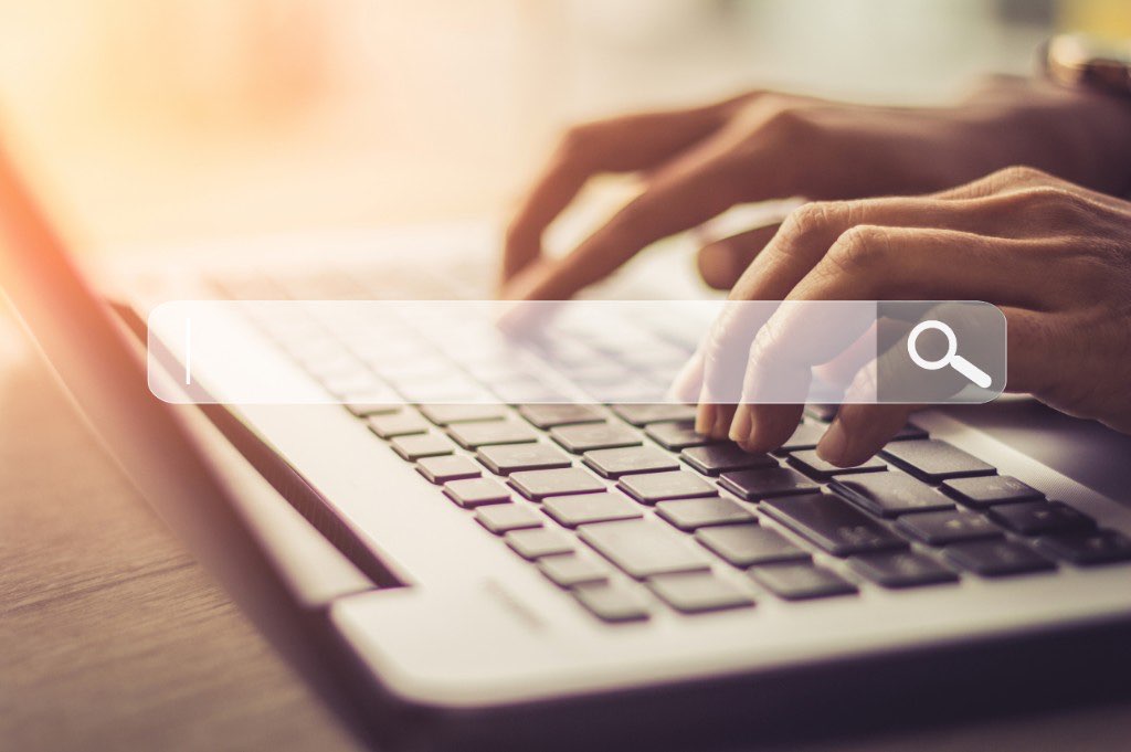 Hands typing on a laptop with a search bar overlay