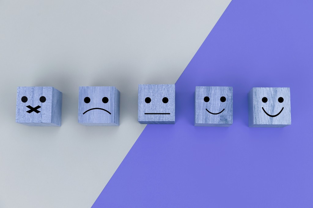 Wooden blocks with drawn faces showing a range of sentiments from negative to positive